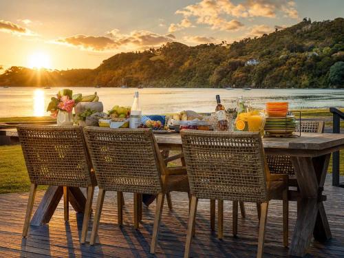 ein Holztisch mit Stühlen und ein Tisch mit Essen darauf in der Unterkunft Blackpool Bayside - Stay Waiheke in Oneroa