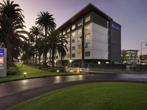 a building with palm trees in front of a street at Novotel Auckland Ellerslie in Auckland