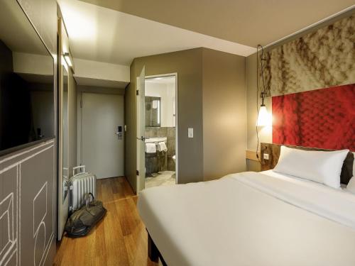 a bedroom with a large white bed and a bathroom at ibis Hotel München Messe in Feldkirchen