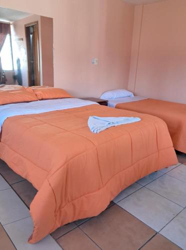 two beds in a room with an orange blanket on them at San Sebastian Hostal in Sangolquí