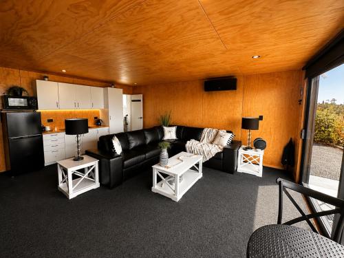 a living room with a black couch and a kitchen at Lake Brunner Chalet in Moana