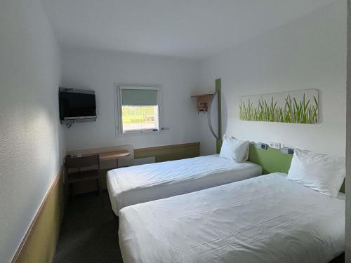 a hotel room with two beds and a television at Ibis Budget Ancenis in Mésanger