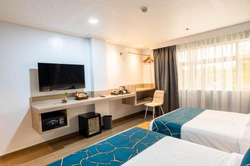 a hotel room with two beds and a desk with a television at Kuadro Hotel & Suites in Moalboal
