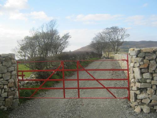 a red gate with a stone wall and a road at Mia's Self Catering Holiday Cottage Donegal in Claggan