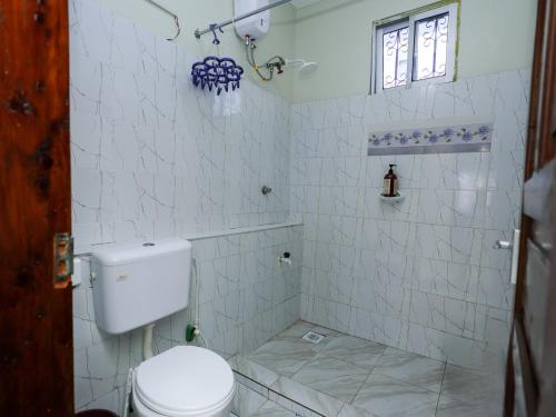a white tiled bathroom with a toilet and a window at Serene Coastal Suites in Mombasa