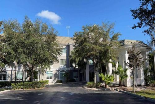 a large white building with trees in front of it at Hotel Flamingo Inn & Suites Vero Beach I-95 in Vero Beach