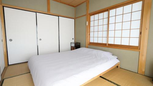 a bedroom with a white bed and three windows at 伊根の宿 汐風 Shiokaze in Nomuro