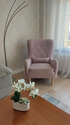 a pink chair in a living room with a table at Apartamentai Gertrūda in Druskininkai