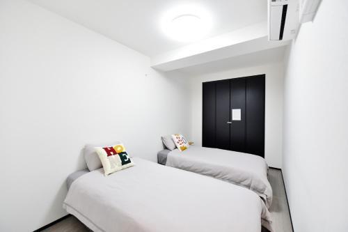 two beds in a room with white walls and a black door at Room 701 Large 3LDK 98sqm Near Namba Big Balcony Ideal for Groups and Long Stay in Osaka