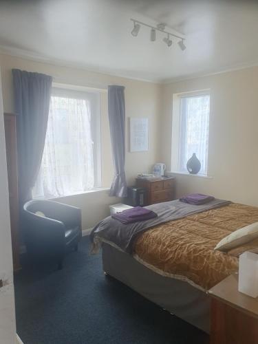 a bedroom with a bed and a chair and windows at Smugglers Rest in Newquay
