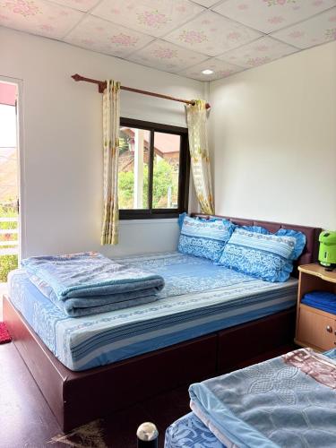 a bedroom with a bed with blue pillows and a window at บ้านพักสมพงศ์ภูทับเบิก in Ban Maeo Thap Boek