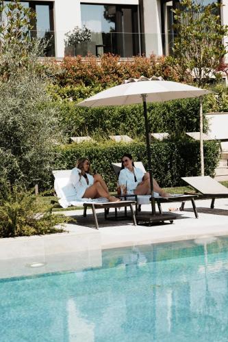 two women sitting on benches next to a swimming pool at THERMA NUMERA Mineral SPA & Longevity in Burgas