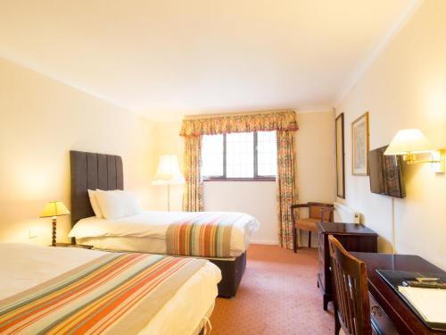 a hotel room with two beds and a desk at The Devil's Punchbowl Hotel in Hindhead