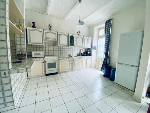 a kitchen with white appliances and a white tiled floor at Le cadeau bleu, duplex en Cévennes in La GrandʼCombe