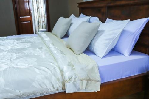 a bed with white sheets and white pillows at Kingram Apartments in Entebbe