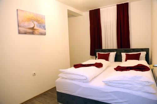 a bedroom with a bed with white sheets and red pillows at City Apartman 103 in Bosanski Brod