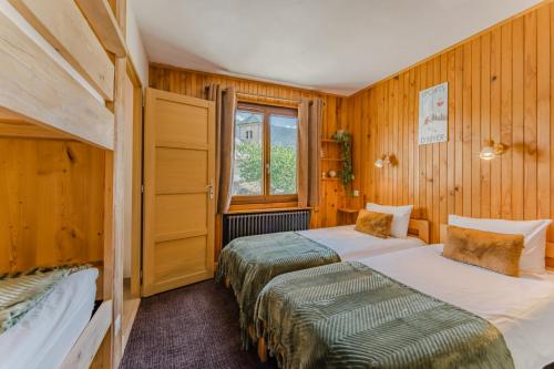 two beds in a room with wooden walls at Le Bellacha in La Léchère