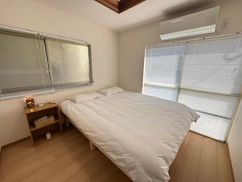 a bedroom with a white bed and two windows at 羽憩館 Hakeikan KIX in Izumi-Sano