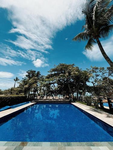 a blue swimming pool with a palm tree at Condo-Resort Juquehy, 4 quartos, em frente ao mar in São Sebastião