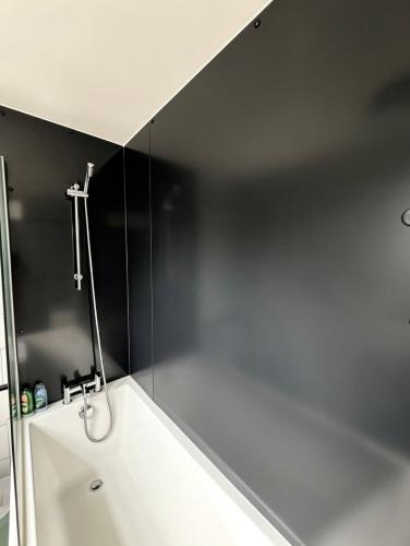a bathroom with a white tub and a black wall at Summerfields cottage stylish Home in Hollington