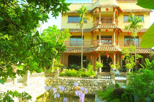 a large yellow house with a stone wall and trees at Y Van Cac Homestay Ninh Binh Art Heritage Rice Field in Ninh Binh