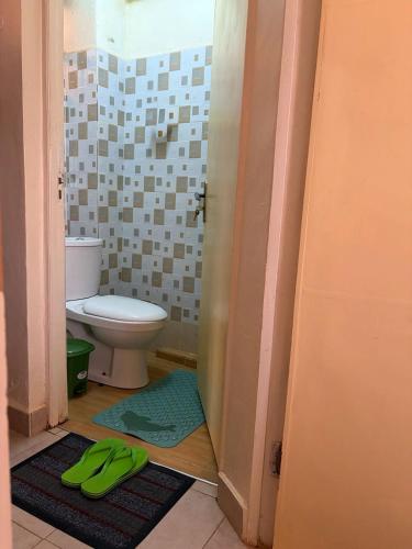a bathroom with a toilet and green slippers on the floor at Tulivu House in Embu