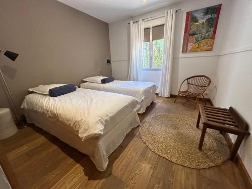 a bedroom with two beds and a chair and a window at Bastide le Petit Clos - les 2 Gîtes in Perpignan