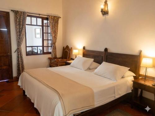 a bedroom with a bed with white sheets and a window at Hotel Mesón de los Virreyes in Villa de Leyva