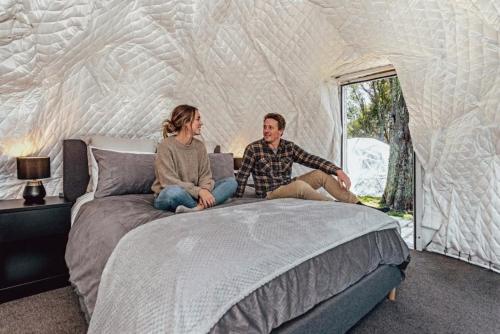a man and woman sitting on a bed in a tent at Black Label Retreats in Gisborne