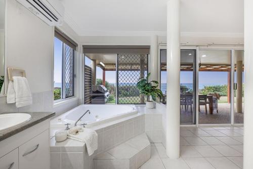 a white bathroom with a tub and a table at Whale Song House in Bargara