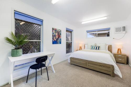 a bedroom with a white bed and a desk at Whale Song House in Bargara