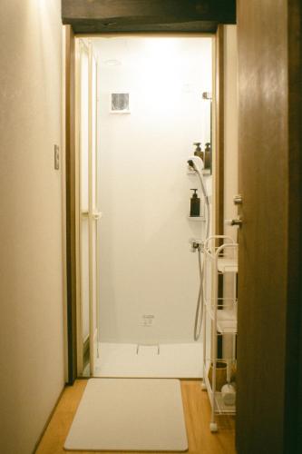 a bathroom with a shower with a white door at サカナギゲストハウス in Nagano