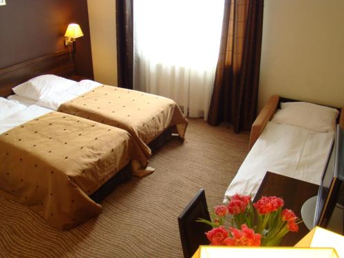a hotel room with two beds and a vase of flowers at Hotel Azalia & Spa in Niepołomice