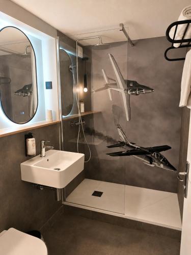 a bathroom with a sink and a shower with planes on the wall at Kyriad Direct Le Bourget Gonesse in Gonesse
