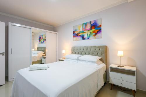 a white bedroom with a large bed and a mirror at Little Britain no centro de Pomerode in Pomerode