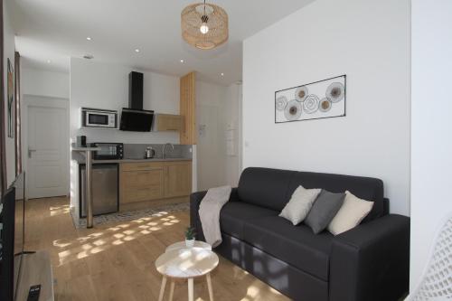 a living room with a black couch and a kitchen at Le Zen by EasyEscale in Romilly-sur-Seine