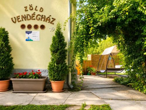 a building with potted plants and a sign on the wall at Zöld Vendégház in Csernely