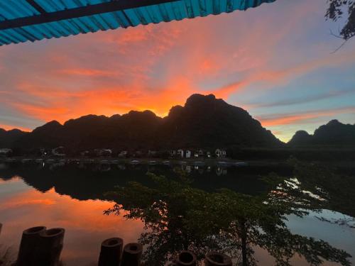 a sunset over the water with a mountain at Phong Nha Coco House - Riverstay & Mountain View in Phong Nha