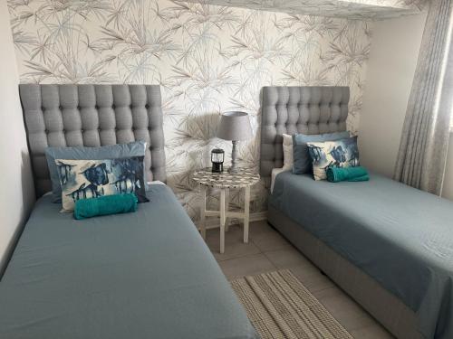 a bedroom with two beds and a table with a lamp at Pebble Moon Holiday Flat in Strand