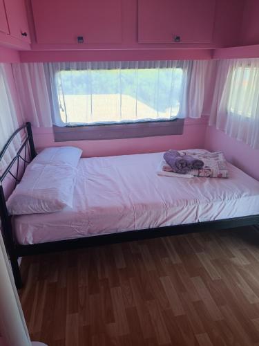a small bed in a pink room with a window at red caravan in Nea Potidaea