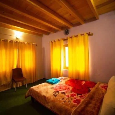 a bedroom with a bed with yellow curtains and a window at Mullberry Lodge Gulmit in Chamangul