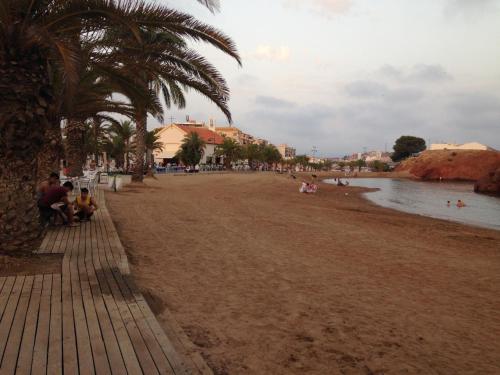 a beach with palm trees and people sitting on the shore at La Isla in Puerto de Mazarrón