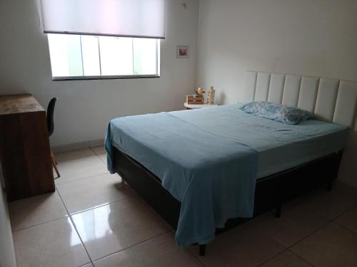 a bedroom with a bed with a blue blanket and a window at Quarto Rustico em Alfenas in Alfenas