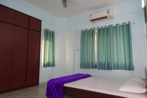 a bedroom with green curtains and a bed with purple sheets at Nalanda Tulip in Kolkata