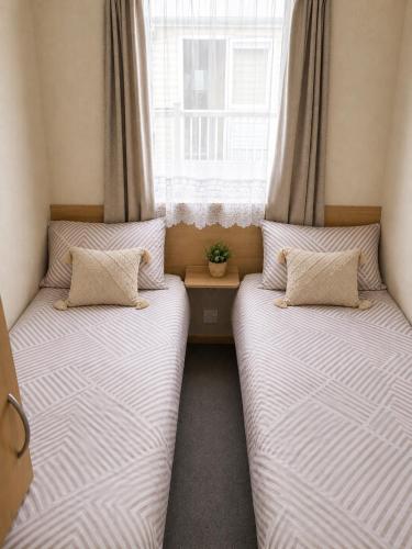 two twin beds in a room with a window at Beachside 3 Bed Caravan with Deck & Outside Seating Mablethorpe in Mablethorpe