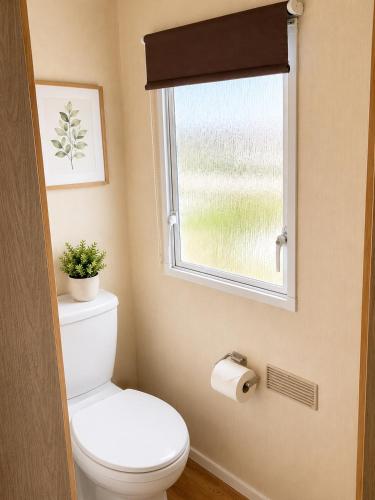 a bathroom with a toilet and a window at Beachside 3 Bed Caravan with Deck & Outside Seating Mablethorpe in Mablethorpe