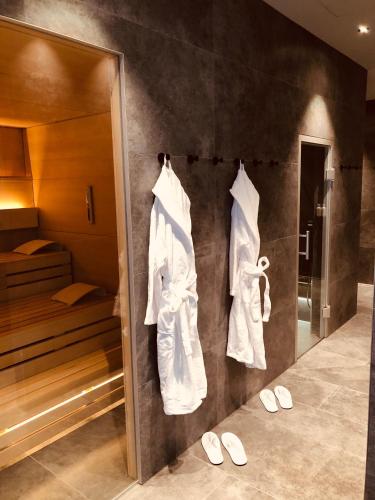 a bathroom with white robes hanging on a wall at SOLLER Business Hotel - Munich Airport MUC in Hallbergmoos