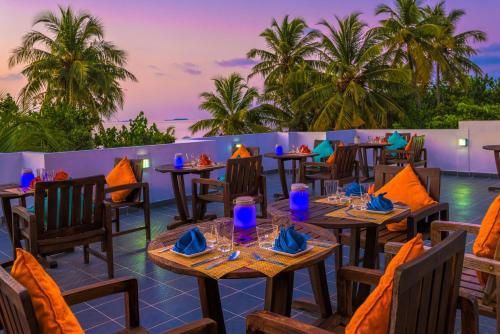 un restaurante con mesas, sillas y palmeras en Boutique Beach All Inclusive Diving Hotel, en Dhigurah