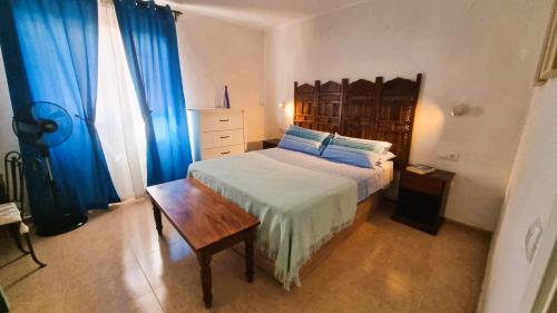 a bedroom with a bed with a wooden table and blue curtains at Apartamento Oasis Tamarindo Vista Al Mar in Corralejo