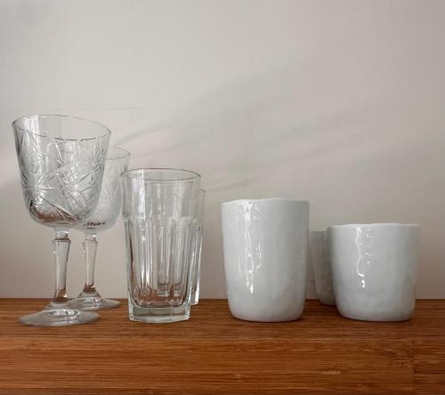 three glasses and three cups sitting on a wooden table at The Lighthouse Cabin in Noordwijk